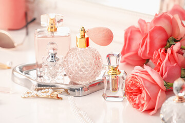 Bottles of different perfumes, accessories and flowers on dressing table indoors, closeup