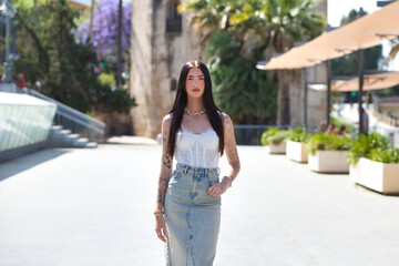 A young, beautiful Latin woman with tattoos on her arms and dressed in casual clothes walks and...
