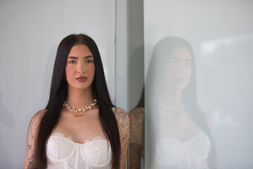 A young, attractive Latin woman with tattoos on her arms, dressed in casual clothes, leaning...