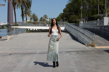 A young, attractive Latin woman with tattoos on her arms and dressed in casual clothes walks and...