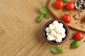Tasty mozzarella balls, tomatoes, peppercorns and basil on wooden table, flat lay. Space for text