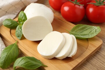 Tasty mozzarella, tomatoes and basil on wooden table, closeup