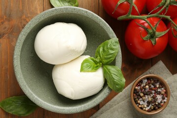 Tasty mozzarella balls, tomatoes and basil on wooden table, flat lay