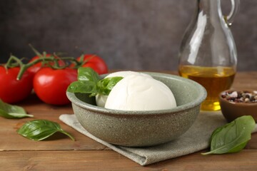 Tasty mozzarella balls, tomatoes, oil and basil on wooden table, closeup