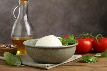 Tasty mozzarella balls, tomatoes, oil and basil on wooden table, closeup