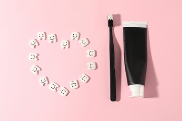 Heart made with teeth figures, toothbrush and paste on pink background, flat lay