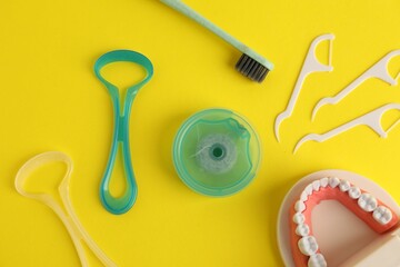 Different oral care products and dental model on yellow background, flat lay