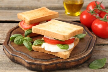 Tasty sandwiches with mozzarella cheese, tomatoes and basil on wooden table, closeup