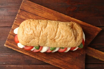 Tasty sandwich with mozzarella cheese, tomatoes and basil on wooden table, top view