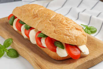 Tasty sandwich with mozzarella cheese, tomatoes and basil on white table, closeup