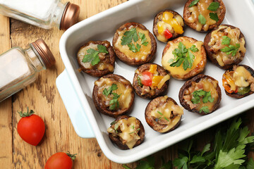 Tasty stuffed mushrooms in baking dish and ingredients on wooden table, flat lay