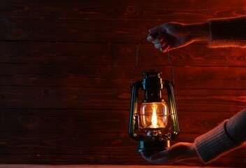 Woman holding vintage kerosene lantern near wooden wall, closeup. Space for text