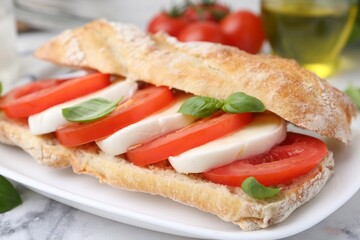 Tasty sandwich with mozzarella cheese, tomatoes and basil on white marble table, closeup