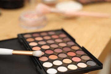 Eyeshadow palette and brush on wooden table, closeup