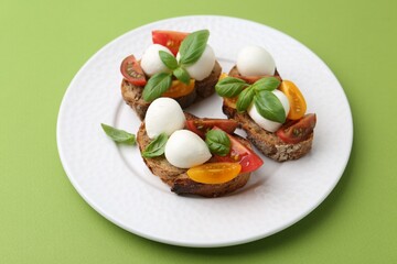 Tasty sandwiches with mozzarella cheese, tomatoes and basil on green background, closeup