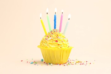 Burning candles in cupcake and sprinkles on beige background