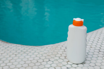 Bottle of sun protection product near swimming pool, space for text