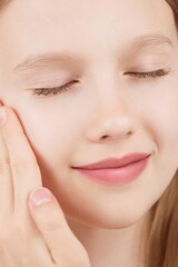 Obraz premium Portrait of smiling cheerful girl doing beauty routine, face massage, applies skin product. Advertisement of self-care products for teenagers. Blonde girl with closed eyes in studio on pink background