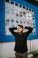Thoughtful young man posing with hands behind head outdoors