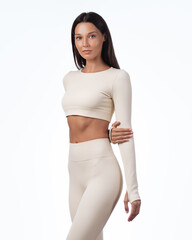 Elegant Woman in Beige Activewear Standing Confidently in Studio Portrait