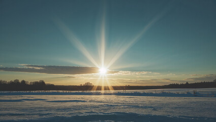 Stunning winter sunrise over snow covered fields with bright sunburst and sky
