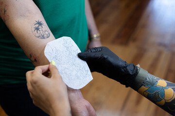 Close-up of a tattoo artist creating a floral tattoo on a woman's hand using a tattoo machine in...