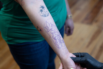 Close-up of a tattoo artist creating a floral tattoo on a woman's hand using a tattoo machine in...