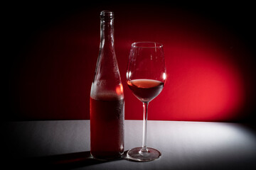 bottle and glass of rosé wine with a red and white background with side lighting