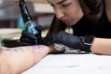 Close-up of a tattoo artist creating a floral tattoo on a woman's hand using a tattoo machine in...