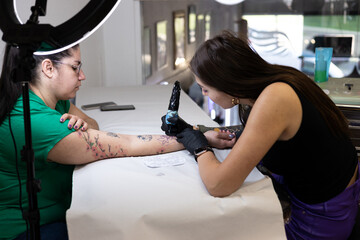 Close-up of a tattoo artist creating a floral tattoo on a woman's hand using a tattoo machine in...