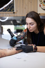 Close-up of a tattoo artist creating a floral tattoo on a woman's hand using a tattoo machine in...