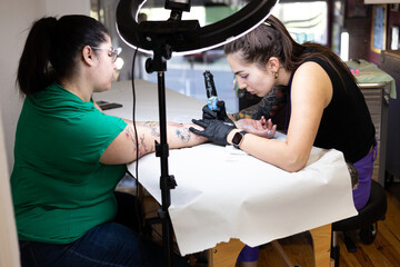 Close-up of a tattoo artist creating a floral tattoo on a woman's hand using a tattoo machine in...