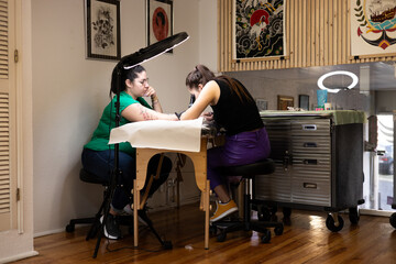 Close-up of a tattoo artist creating a floral tattoo on a woman's hand using a tattoo machine in...