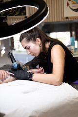 Close-up of a tattoo artist creating a floral tattoo on a woman's hand using a tattoo machine in...