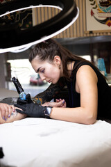 Close-up of a tattoo artist creating a floral tattoo on a woman's hand using a tattoo machine in...