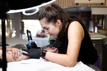 Close-up of a tattoo artist creating a floral tattoo on a woman's hand using a tattoo machine in...