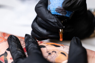 Fototapeta premium Close-up of a tattoo artist creating a floral tattoo on a woman's hand using a tattoo machine in studio.