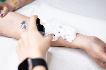 Close-up of a tattoo artist creating a floral tattoo on a woman's hand using a tattoo machine in...