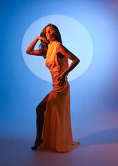 creative portrait of a female model wearing a glamorous yellow fashion ball gown. elegantly posing on studio background with dramatic colourful  lighting