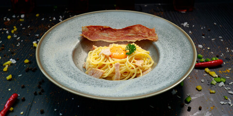 close up of a plate of pasta carbonara with a slice of bacon 