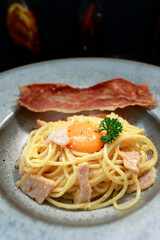 close up of a plate of pasta carbonara with a slice of bacon 