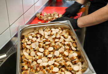 Sliced German sausages being prepared in a professional kitchen. A chef with gloves cuts bratwurst into bite-sized pieces for catering or traditional buffet service.