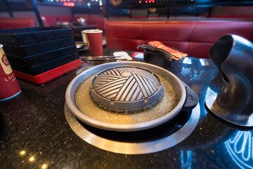Obraz premium Korean BBQ grill pan on a table in a restaurant with metal grill and broth around, ready for cooking with condiments nearby