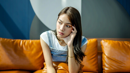 Obraz premium Sad woman sitting on sofa at home deep in thoughts, thinking about important things, she is lonely and sad, trying relaxing in living room