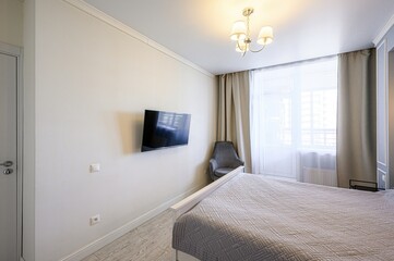 cozy bedroom with a bed, a chair, curtains, and a TV. The room has soft lighting from lamps and...