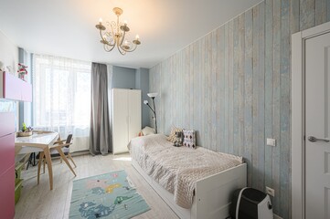 Cozy bedroom with single bed, desk, wardrobe, and world map rug. Soft blue walls and bright accents create a playful atmosphere