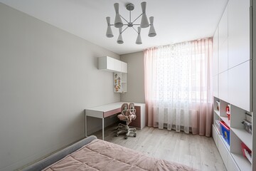 Bright child's room with desk, pink accents, white storage, and a modern chandelier. A bed is partially visible