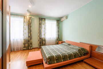 cozy bedroom features a large wardrobe with sliding doors, a bed with a patterned comforter, and windows with green floral curtains. The walls are light green