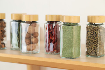 Many different aromatic spices in jars on wooden shelving unit indoors, closeup