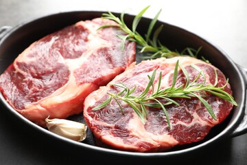 Pieces of raw beef meat and spices in baking dish on gray table, closeup